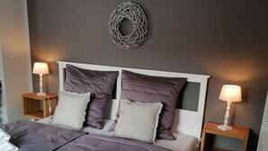 Una cama impecablemente hecha con una combinación de colores gris y blanco, dos mesitas de noche con lámparas y un adorno en la pared.