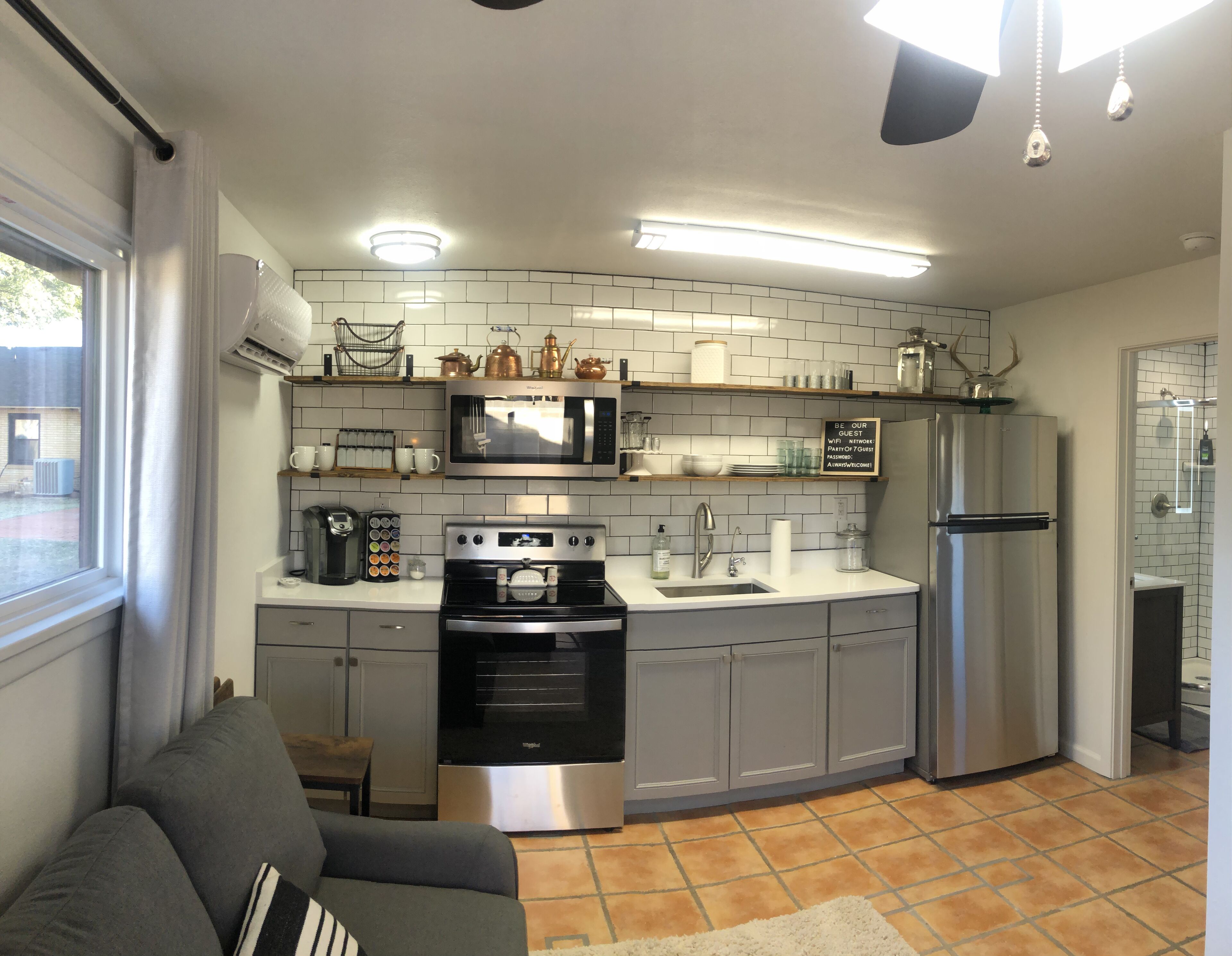 A compact kitchen with a microwave, stove, and refrigerator. There is a window with curtains, a sink, and a countertop with various items.