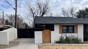 Une petite maison à un seul étage, avec un toit noir, des murs en briques blanches et un portail en bois.