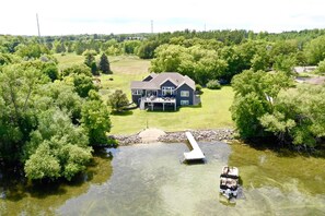 Una casa grande con un muelle que se adentra en un lago, rodeada de abundante vegetación.