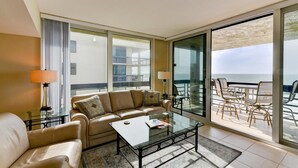 A spacious living room with a sofa, coffee table, and a balcony with outdoor seating. - Full Beachfront 2 BR Condo (Longboat Key)