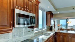 A modern kitchen with wooden cabinets, stainless steel appliances, and a large window providing a view of the ocean. - Full Beachfront 2 BR Condo (Longboat Key)