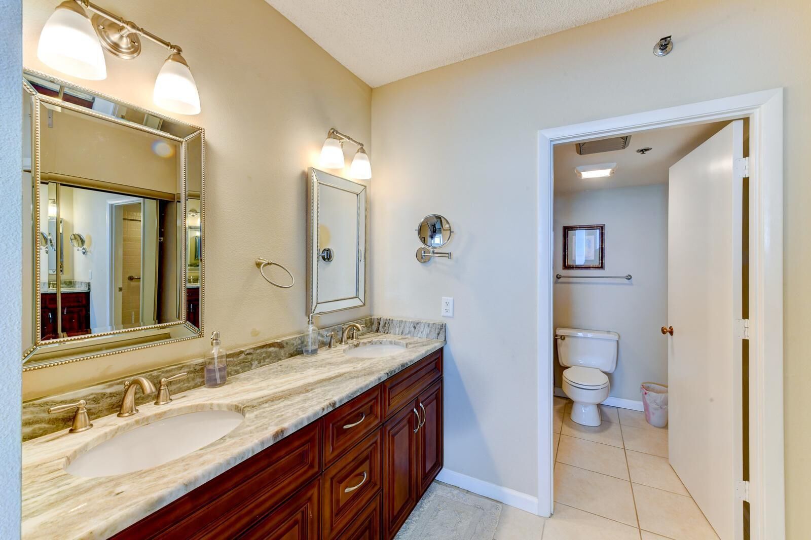 Une salle de bain avec un meuble-lavabo à deux vasques, un grand miroir et des toilettes visibles à travers une porte ouverte.