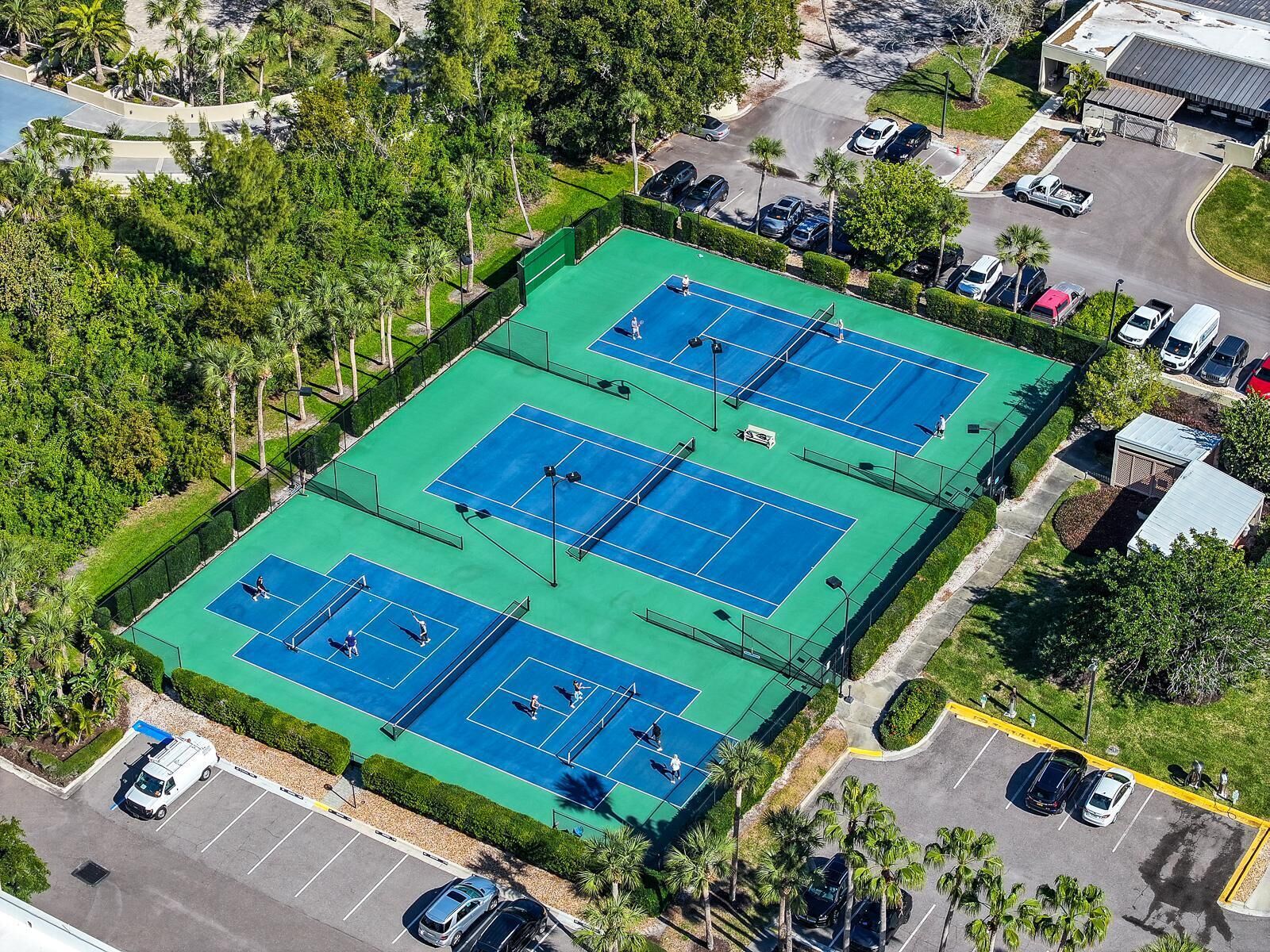 En vy från ovan av ett tennisanläggningsområde med flera banor, omgivet av parkeringsplatser och grönområden.
