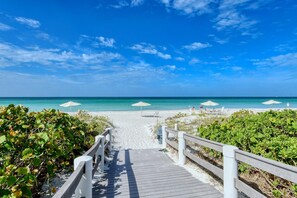 A wooden boardwalk leading to a beach with umbrellas and lounge chairs. - Full Beach View 2 Bedroom Condo (Longboat Key)