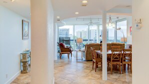 A spacious living area with a dining table, chairs, and a sofa. There is a large window providing a view of the cityscape. - Great Beach View 2 Bedroom Condo (Longboat Key)