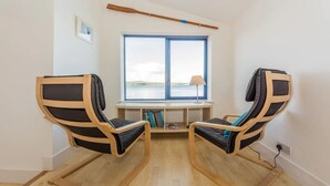 A room with two wooden chairs with black cushions, a small table with a lamp, and a window with a view of the sea. - Mulroe Cove - The Boathouse, Fisherman's Lane (Mulroe)