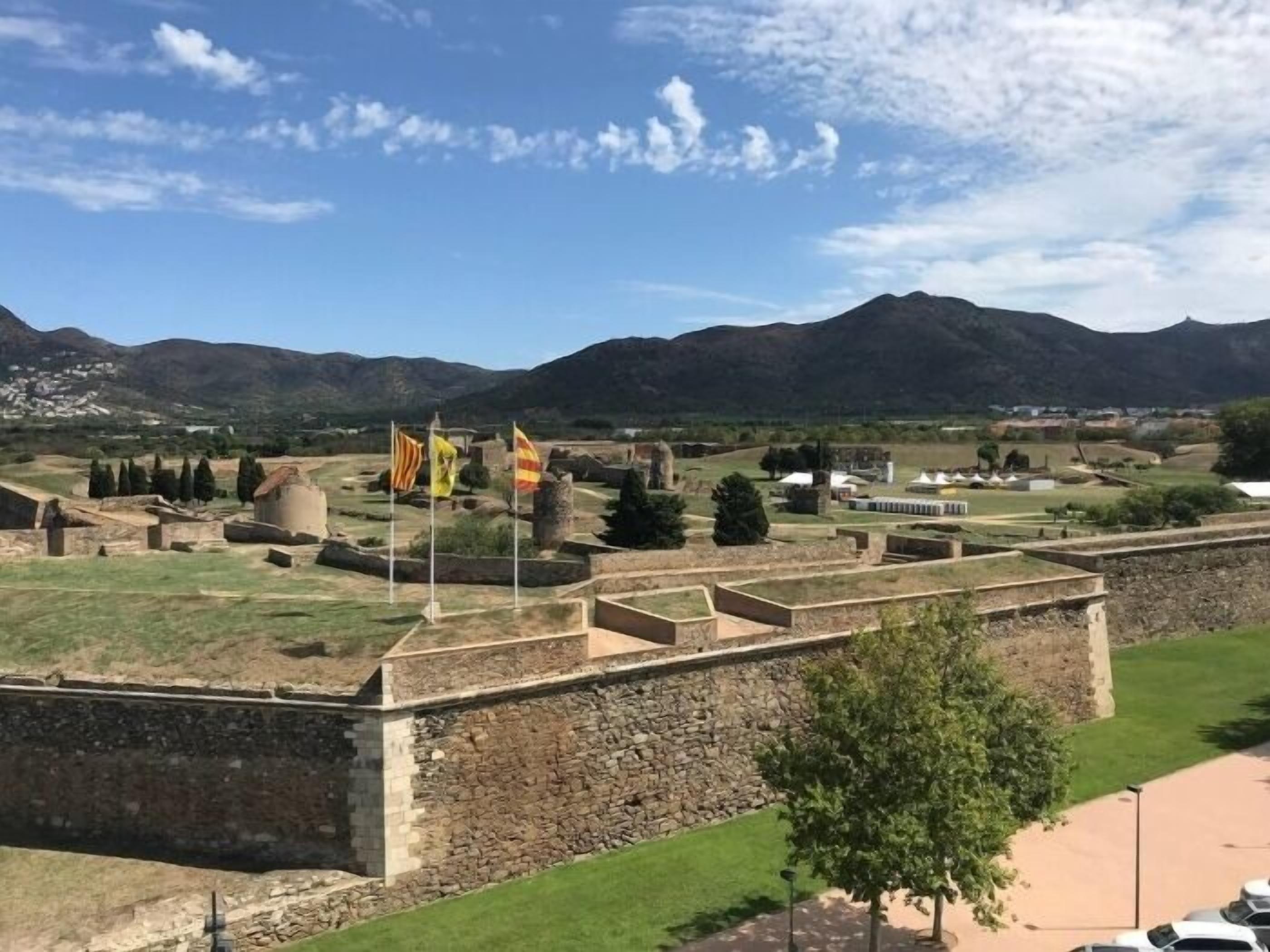 A historic fort with stone walls, flags, and a mountainous backdrop.