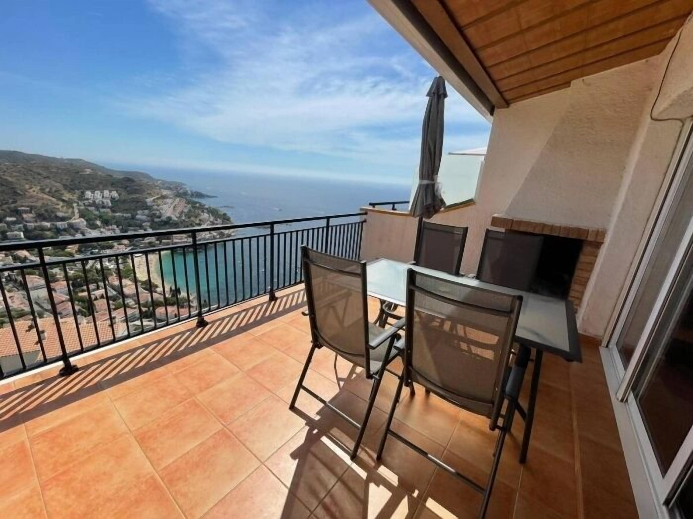 Un balcón con mesa y sillas, una parrilla y vistas al mar y las colinas.