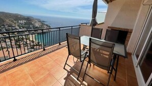 Un balcón con mesa y sillas, una parrilla y vistas al mar y las colinas.