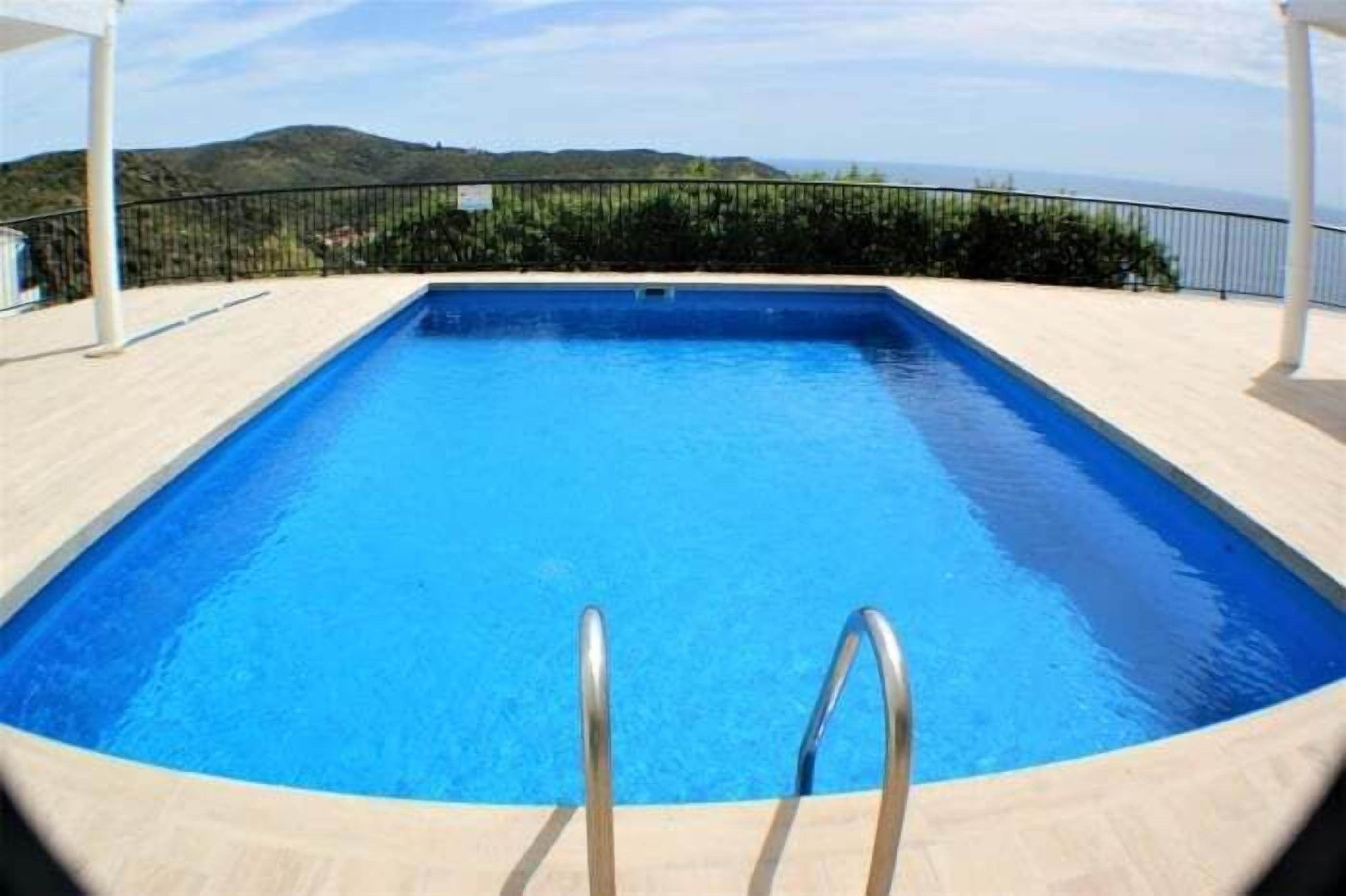 A rectangular swimming pool with clear blue water, surrounded by a light-colored deck and metal railings.