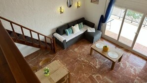 Un salón con sofá, una mesa de comedor con sillas, una escalera y un ventanal con vistas.