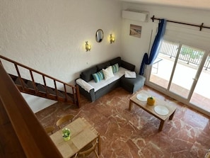 A living room with a sofa, a dining table with chairs, a staircase, and a large window with a view.