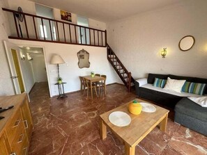 A spacious living area with a wooden dining table, a sofa, and a staircase leading to an upper floor.