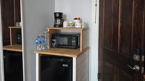 A compact kitchenette with a coffee maker, microwave, and water bottles on a wooden shelf. - The Pollock Suite is one of our four rooms. (Hermann)