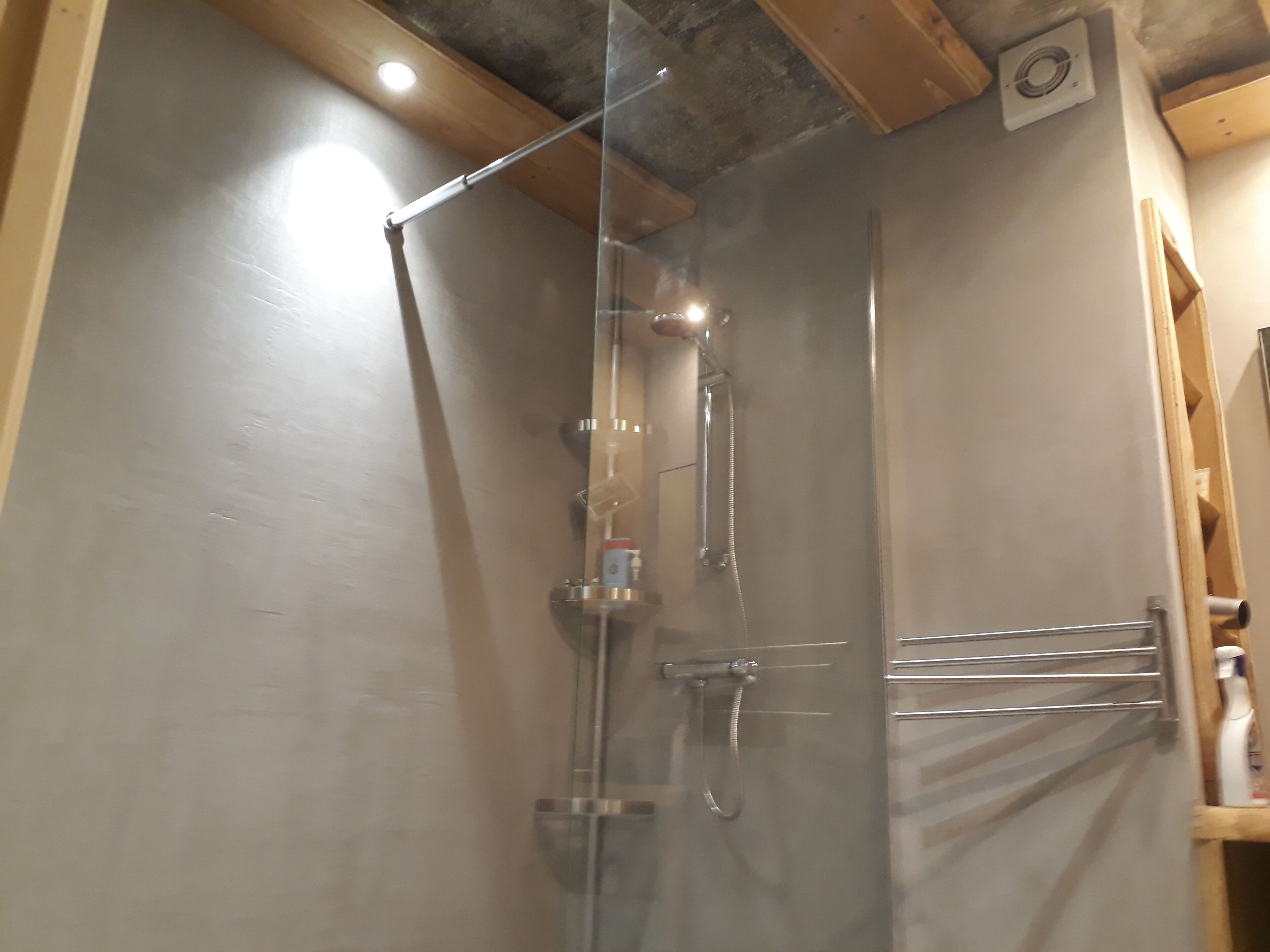 A shower with a glass door, a handheld showerhead, and a wall-mounted faucet.