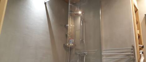 A shower with a glass door, a handheld showerhead, and a wall-mounted faucet.