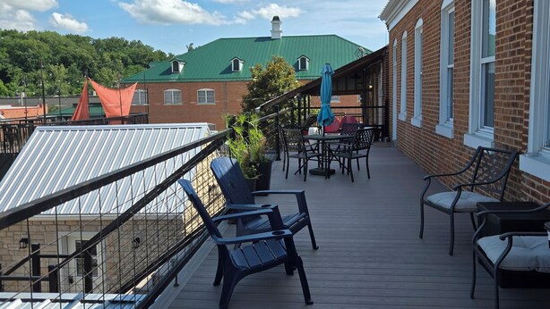 A wooden deck with outdoor furniture, a brick building with arched windows, and a green-roofed structure in the background.