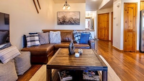A living room with a brown leather sofa, a wooden coffee table, and a painting on the wall. - Lookout Ridge Townhomes #113 by Summit County Mountain Retreats (Dillon)