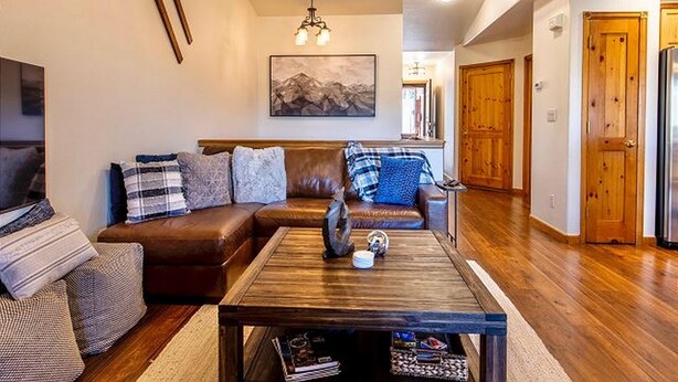 A living room with a brown leather sofa, a wooden coffee table, and a painting on the wall. - Lookout Ridge Townhomes #113 by Summit County Mountain Retreats (Dillon)