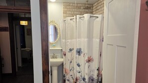 A bathroom with a wooden floor, a white toilet, a sink, and a shower with floral curtains. - The Monet Suite is one of our four rooms. (Hermann)