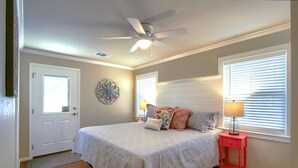 A bedroom with a bed, a ceiling fan, a nightstand with a lamp, and a window with blinds.