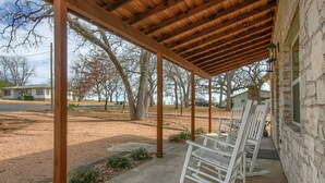 A covered outdoor area with a concrete floor, wooden beams, and white rocking chairs.