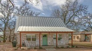A stone building with a metal roof, a green door, and white chairs outside.