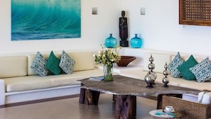 A living room with a large wave painting, a sofa with patterned cushions, a coffee table with a vase of flowers, and decorative items. - PAY 6 STAY 7 NIGHTS until Oct 31. Luxury Villa at Conchas Chinas w/ Ocean Views (Puerto Vallarta)