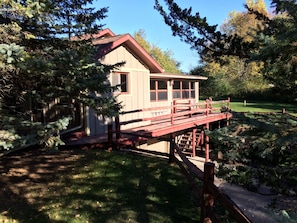 Situated in a lush environment, this cabin features a charming front porch and a serene natural setting surrounded by tall evergreen trees.