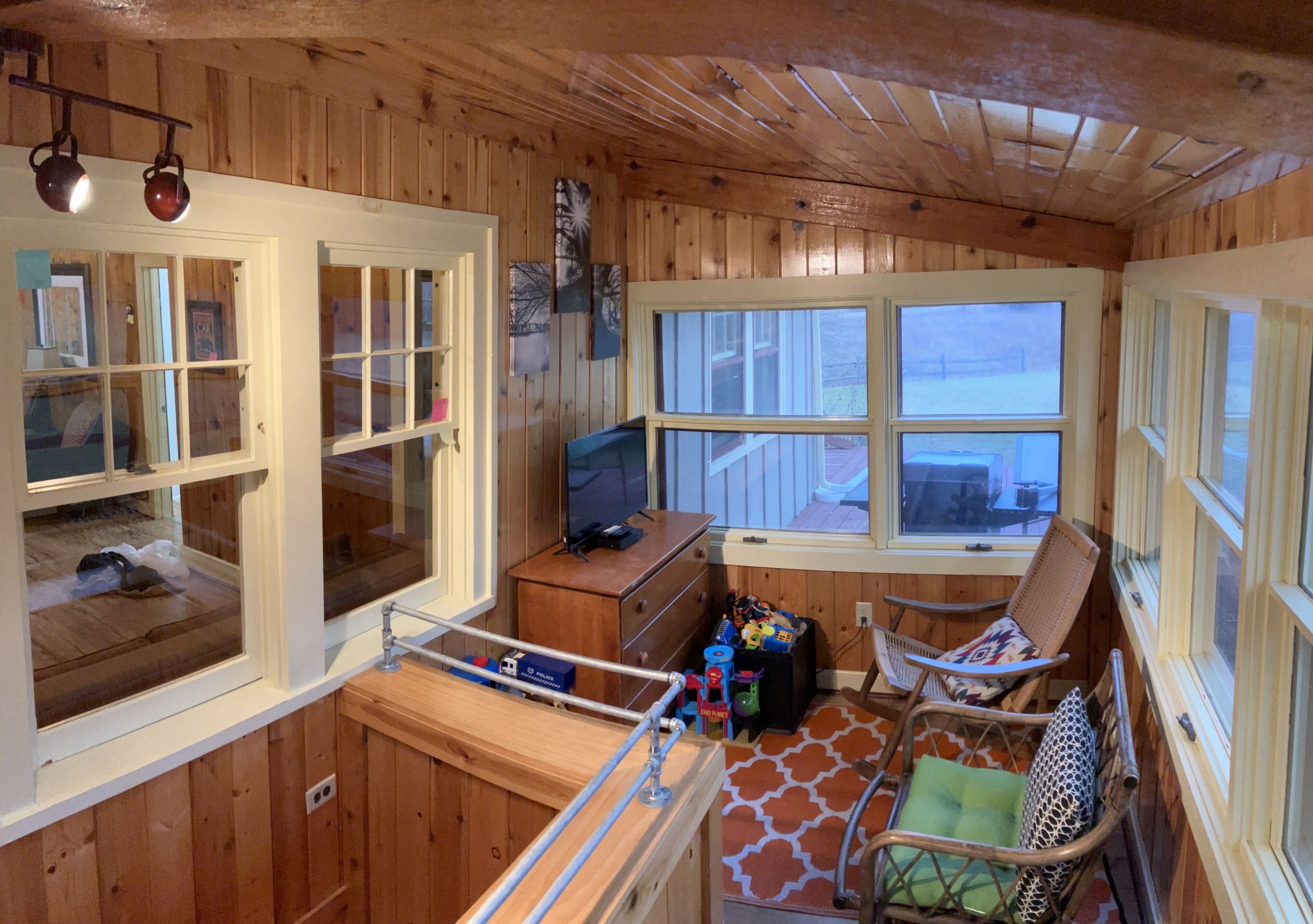 A cabin with wooden walls, a TV, a desk, and two chairs.