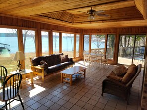 Un cuarto acogedor con techo de madera, ventanas amplias con vistas a un lago, un sofá, una mesita de centro y una mesa de comedor con sillas.