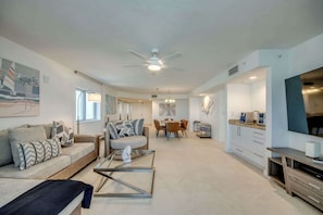A modern living room with a sofa, coffee table, and dining area. - Ocean Harbor #1005B Spacious Bayfront Condo (Fort Myers Beach)