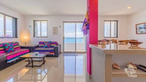 A modern living room with a sofa set, a coffee table, and a view of the sea through a glass door. - Casa Perla Suite 2 : Caribbean Oceanfront 2 Bdrm w/rooftop dipping pool (Mid Island)