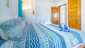 A bedroom with a patterned bedspread, a wooden door, and a ceiling fan. - Casa Perla Suite 2 : Caribbean Oceanfront 2 Bdrm w/rooftop dipping pool (Mid Island)