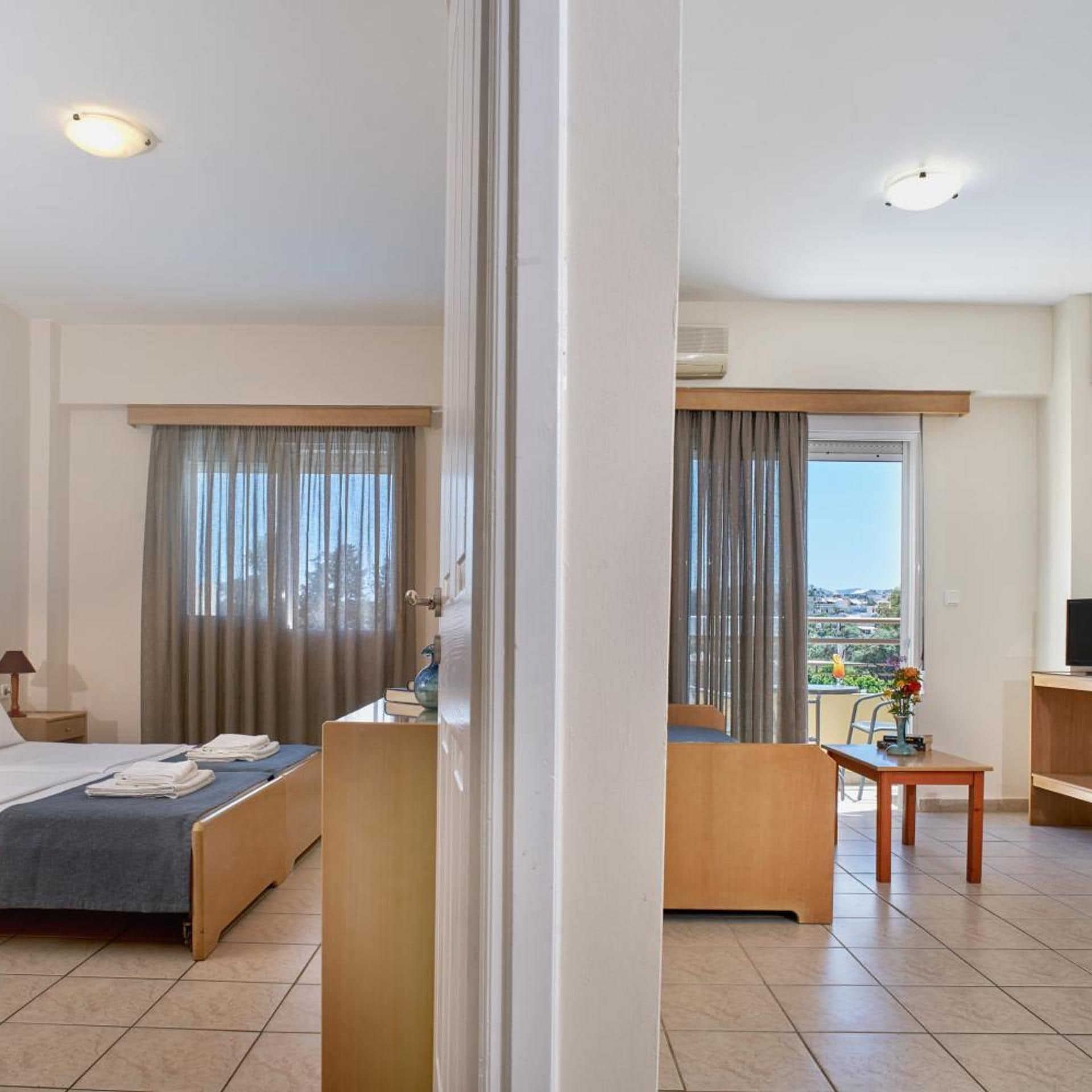 Quarto de hotel com cama, escrivaninha, cadeira, televisão e varanda com vista.