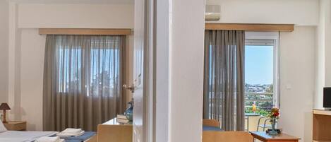 Quarto de hotel com cama, escrivaninha, cadeira, televisão e varanda com vista.