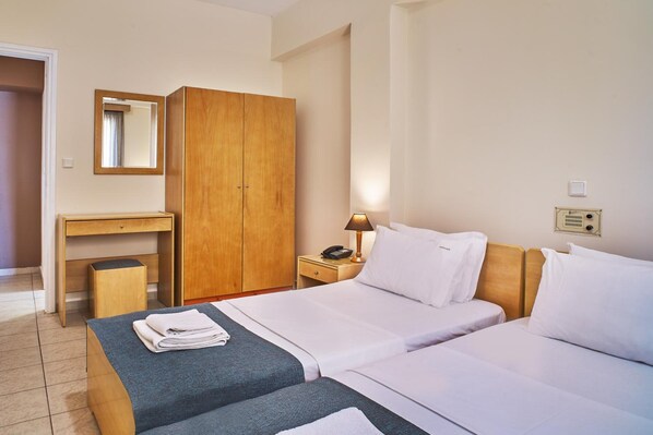 A hotel room with two beds, a wooden wardrobe, a desk with a mirror, a nightstand with a lamp, and a telephone. - Veronica Hotel (Chania)