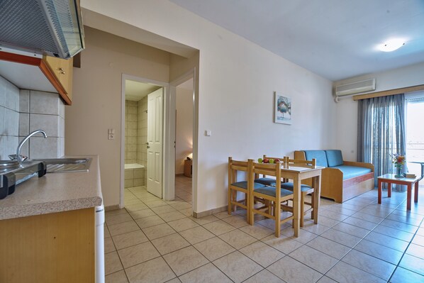 A kitchen with a sink and countertop, a dining area with chairs and a table, a sofa, and a small table with a vase. - Veronica Hotel (Chania)