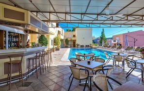 Uma área de piscina ao ar livre com espreguiçadeiras e mesas, um bar com garrafas e uma área de estar coberta.
