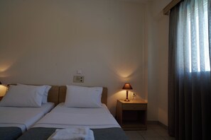 A hotel room with two single beds, a bedside table with a lamp, and a window with curtains. - Veronica Hotel (Chania)