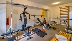 Un gimnasio con equipo de ejercicio, una banca, una plataforma elevada y una escalera de madera.