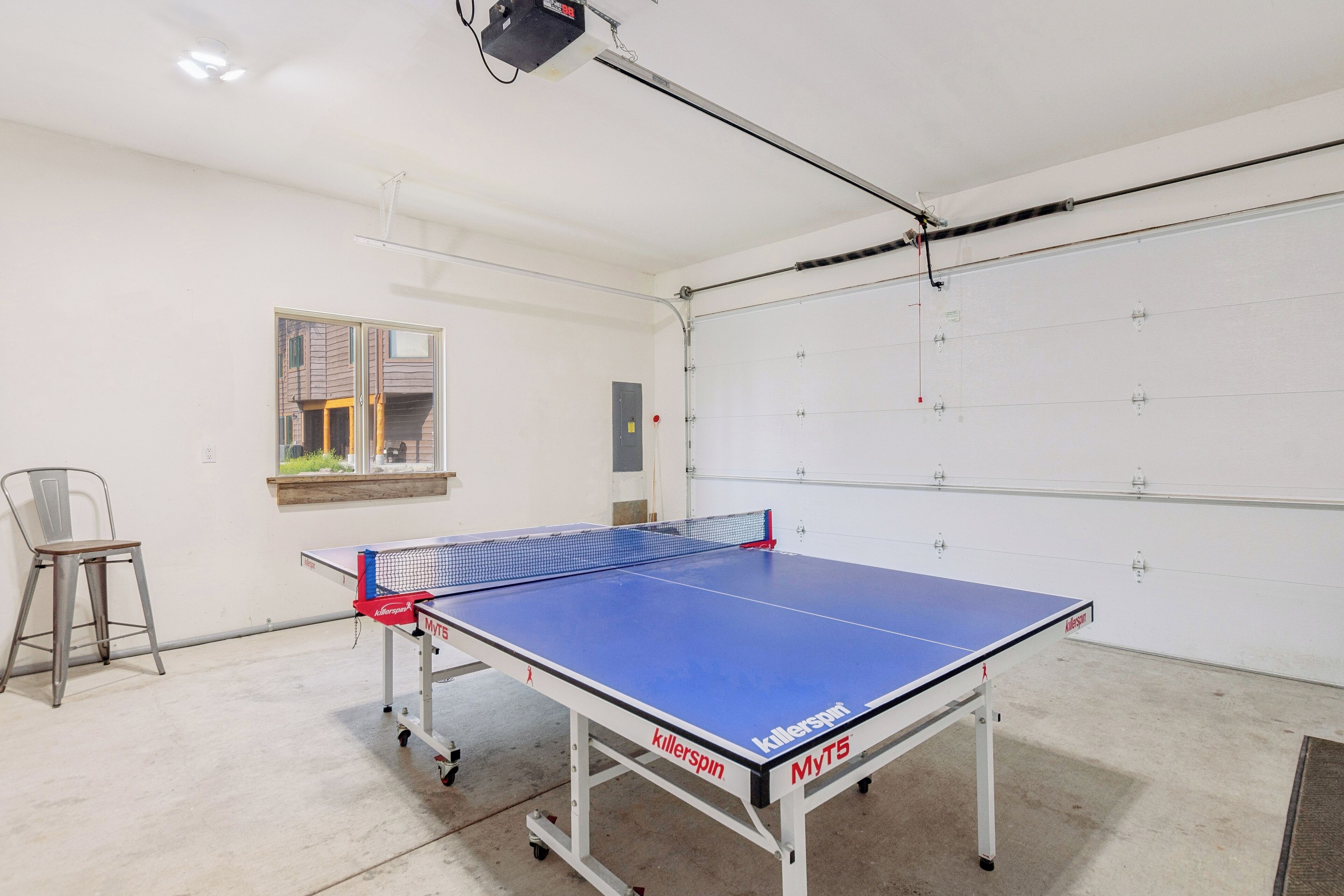 A ping pong table in a room with a white door, a window, and a chair.