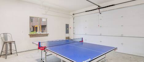 A ping pong table in a room with a white door, a window, and a chair.