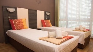 A hotel room with two beds, each with a white bedspread, red and orange patterned pillows, and neatly folded towels. - Elite Apartments Complex II III IV (Sunny Beach)