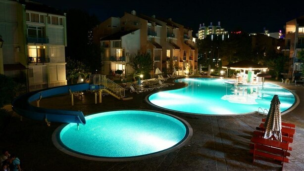 A swimming pool area at night with multiple pools, lounge chairs, and a water fountain. - Elite Apartments Complex II III IV (Sunny Beach)