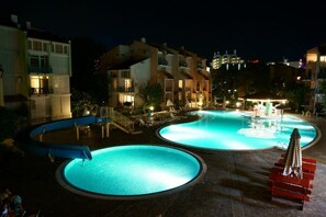A swimming pool area at night with multiple pools, lounge chairs, and a water fountain. - Elite Apartments Complex II III IV (Sunny Beach)