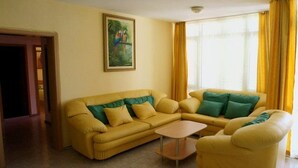 A living room with a yellow sofa set, a small coffee table, and a painting of parrots on the wall. - Elite Apartments Complex II III IV (Sunny Beach)