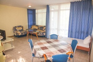 A compact living room with a round table, blue chairs, a sofa, and a bed. - Elite Apartments Complex II III IV (Sunny Beach)
