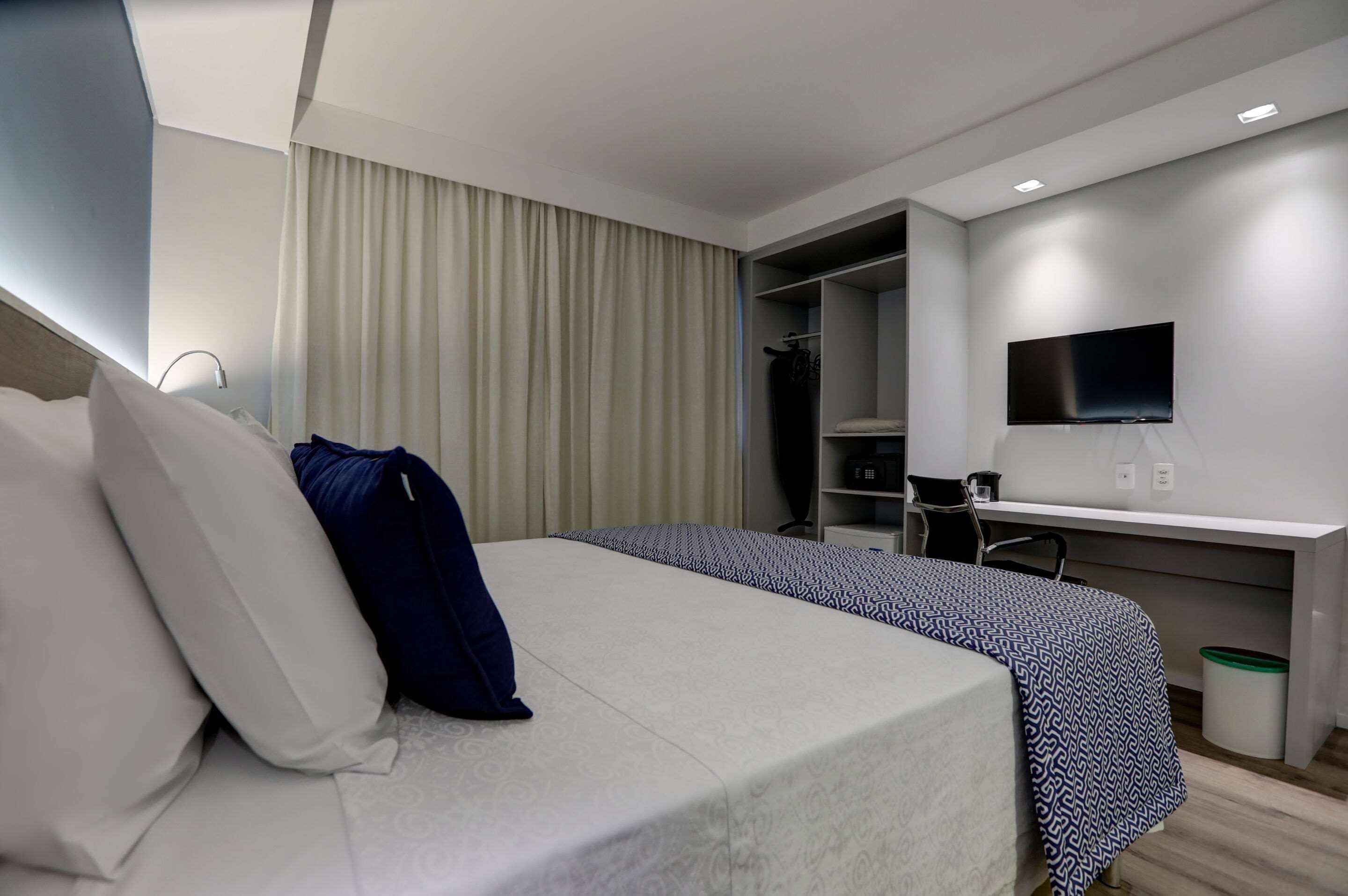 A modern hotel room with a bed, a desk, a TV, and a wardrobe.